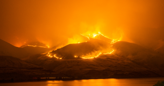 Paysage de montagnes en feu illuminé d’une lumière orange intense, évoquant la chaleur et l’intensité, un parallèle avec les rougeurs et irritations de la peau causées par des sensibilités accrues.