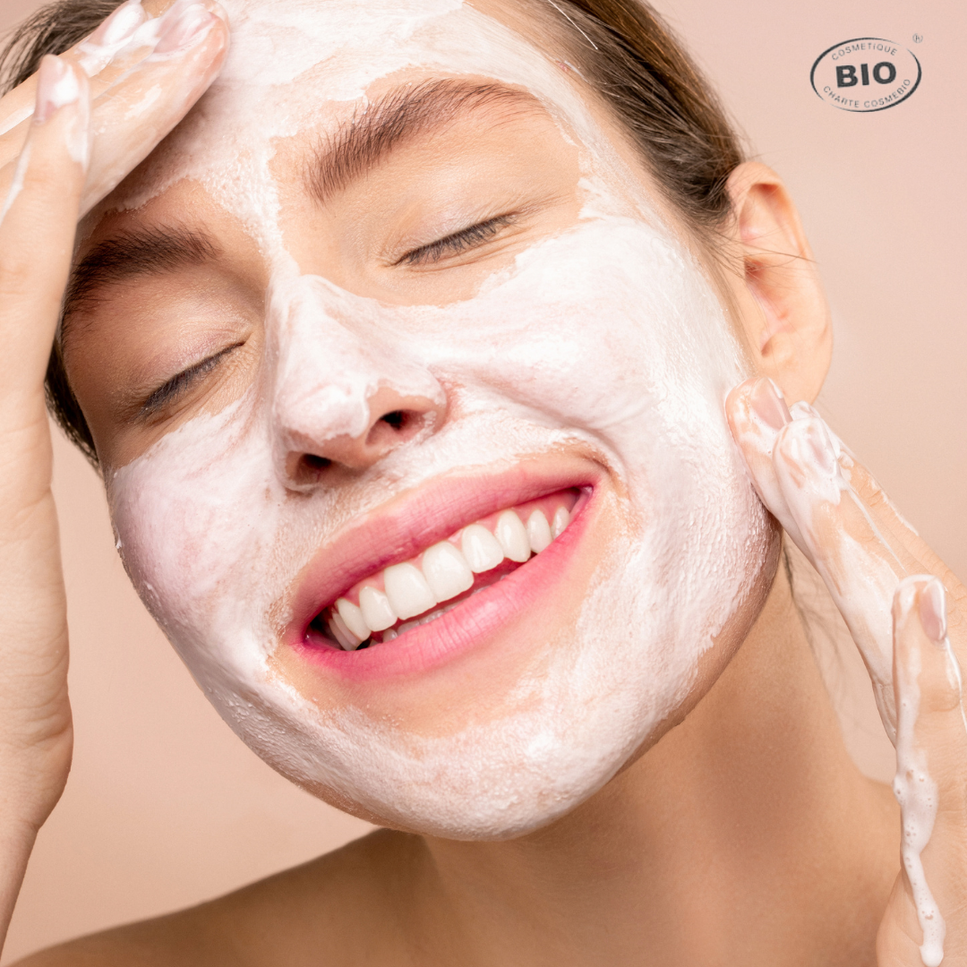 Jeune femme souriante appliquant un masque visage bio moussant pour nettoyer la peau en profondeur tout en douceur avec des soins certifiés naturels.