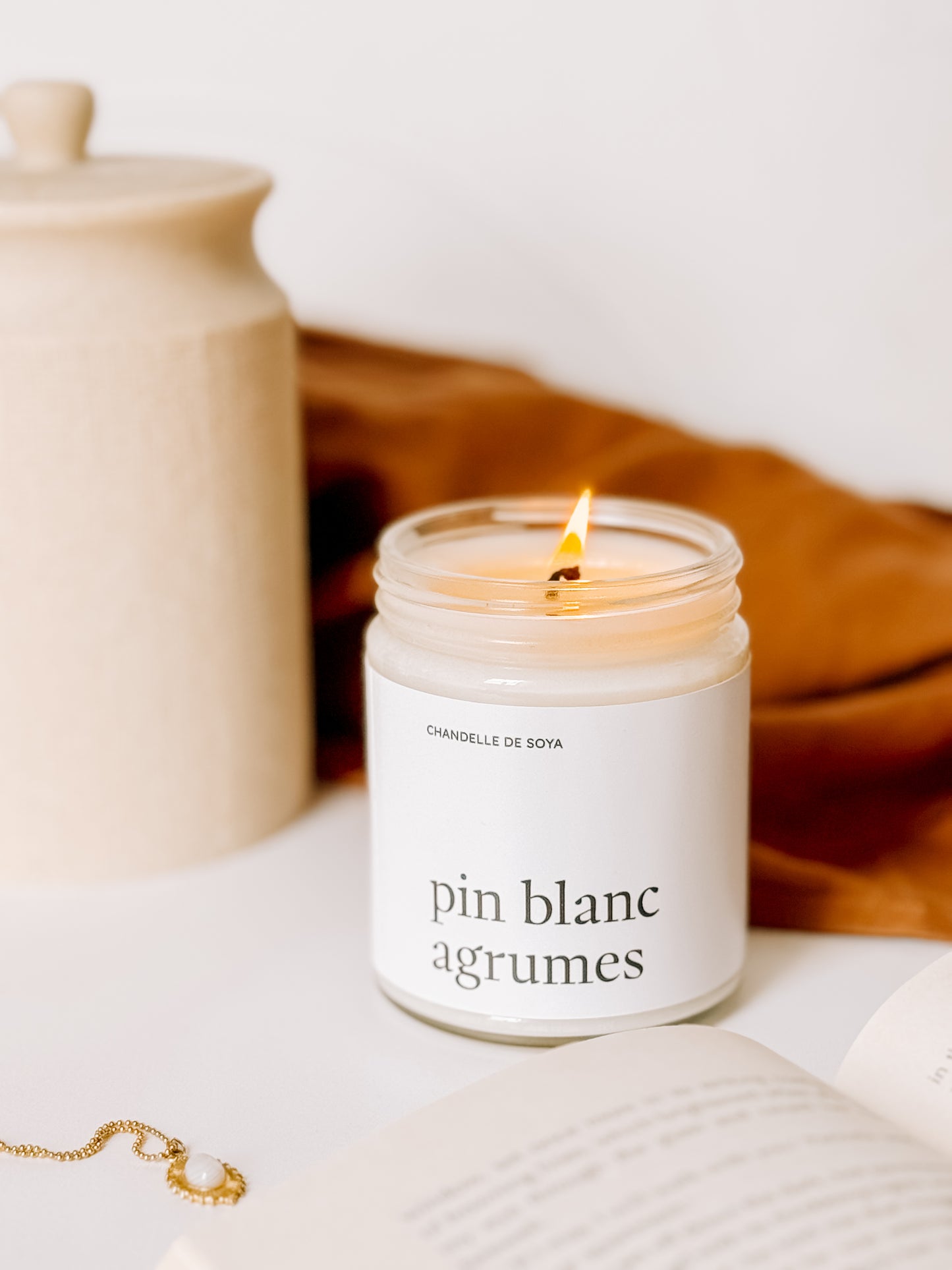 Chandelle en cire de soya au parfum de pin blanc et agrumes, posée allumée sur une surface blanche avec un arrière-plan chaleureux.