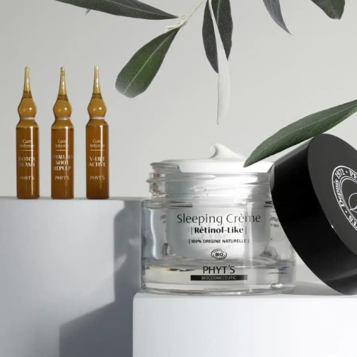 Pot de Sleeping Crème Retinol-Like de Phyt’s posé près de trois ampoules booster anti-âge et d’une branche d’olivier, sur fond élégant et naturel.