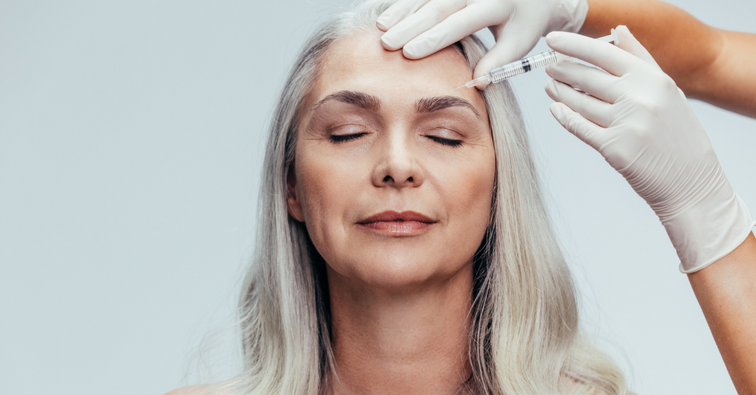 Femme mature aux cheveux gris recevant une injection esthétique sur le front, illustrant l'usage des injectables après 40 ans pour lisser les rides et raffermir la peau.