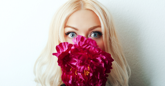 Femme qui se cache le bas du visage, derrière un bouquet de fleurs rose/rouge représentant de l'acné d'adulte sur le bas du visage. 