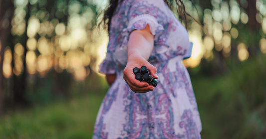 Femme au crépuscule tenant des bouteilles d'huiles essentielles pour démontrer l'usage estival.