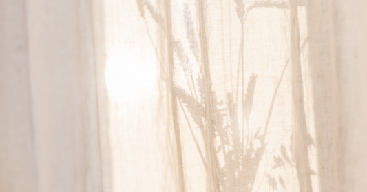 Soleil et plante derrière un rideau beige faisant allusion à la protection solaire large spectre pour la peau