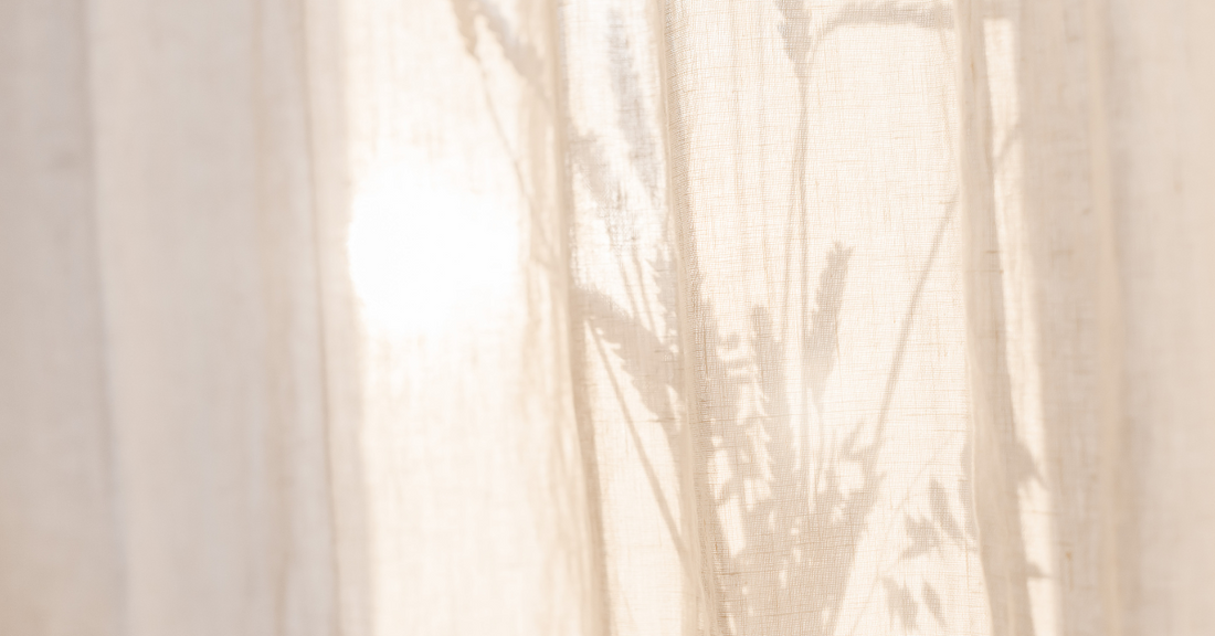Soleil et plante derrière un rideau beige faisant allusion à la protection solaire large spectre pour la peau