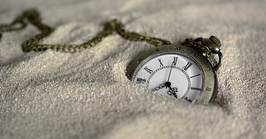 Montre ancienne partiellement enfouie dans le sable, illustrant le passage du temps et la nécessité de prendre soin de soi pour préserver la peau.