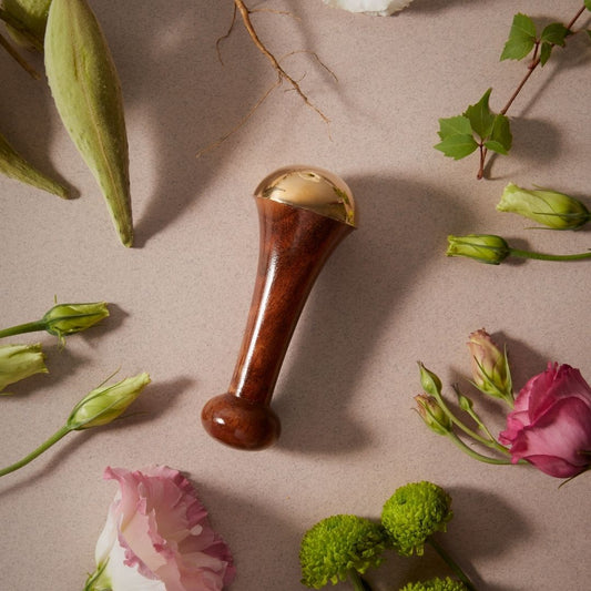 Kansa Wand en bois et alliage de métal doré entouré de fleurs fraîches, idéal pour un rituel de beauté holistique.