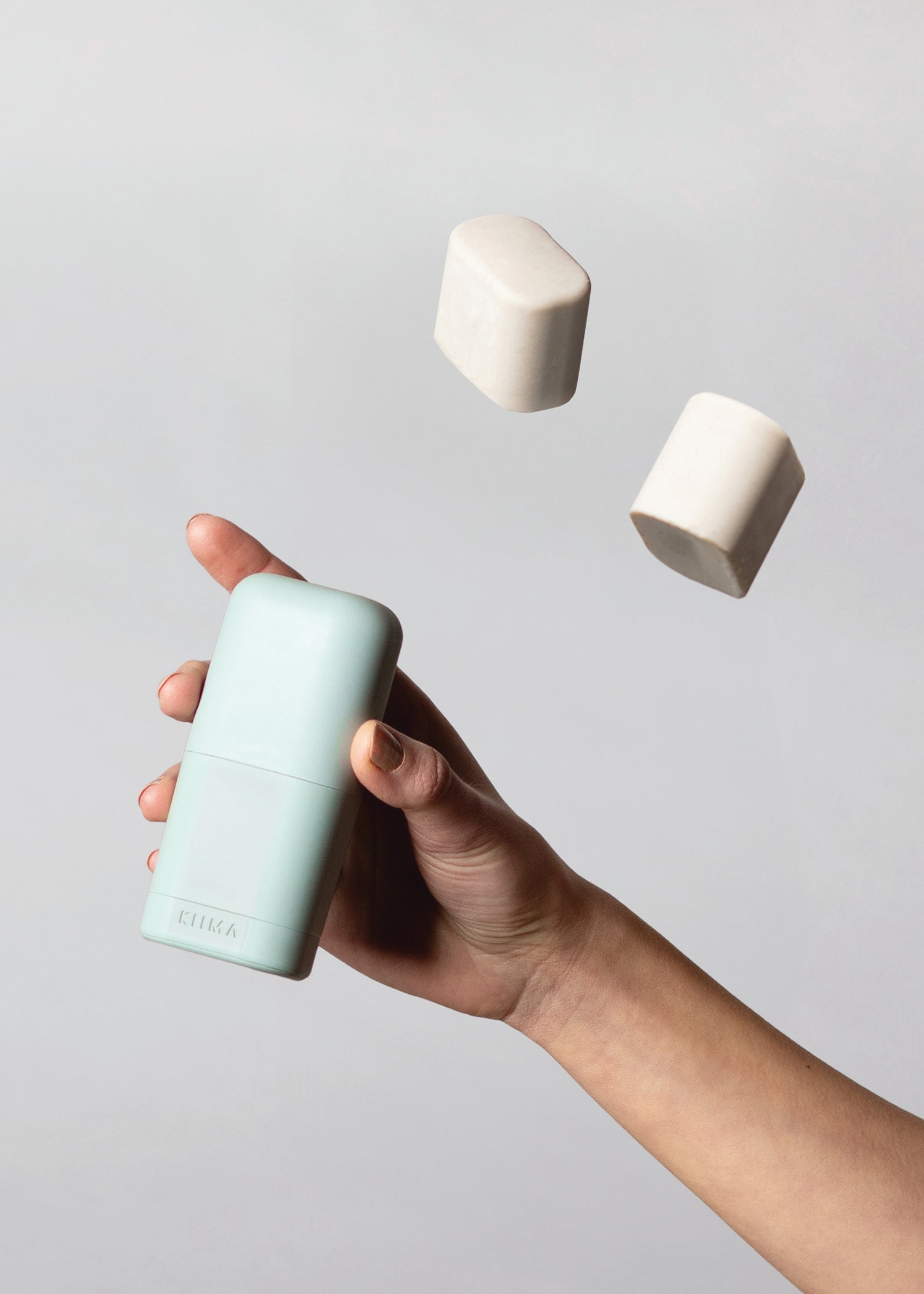 Main tenant un applicateur de déodorant rechargeable KIIMA avec recharges solides en suspension, mettant en valeur le concept rechargeable et zéro déchet.
