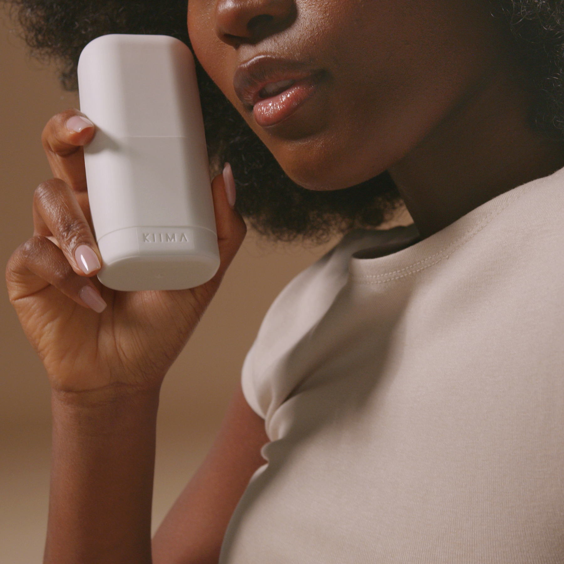 Femme utilisant un applicateur de déodorant rechargeable KIIMA blanc, symbole d’une routine de soins corporels naturelle.