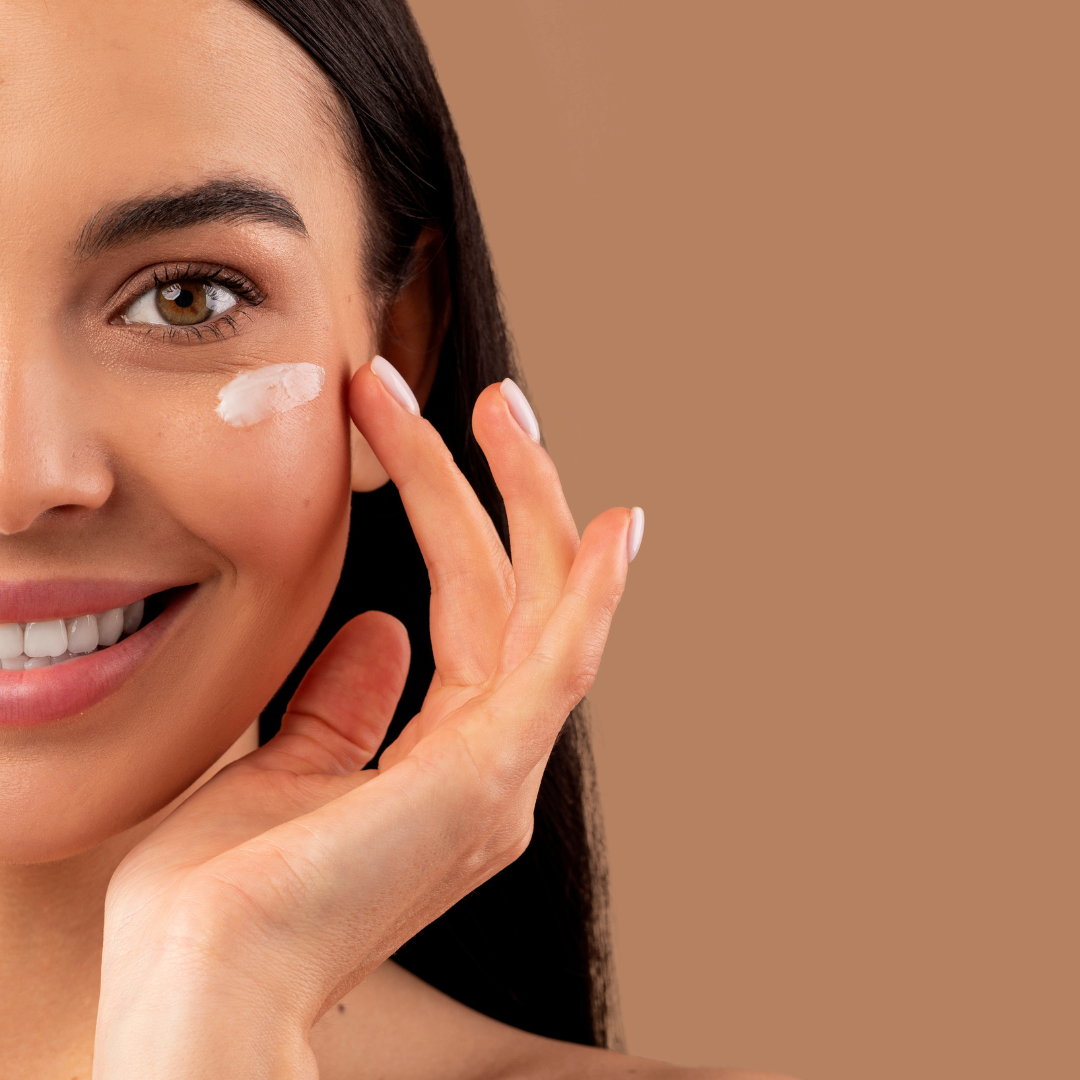 Une femme applique délicatement une crème hydratante autour des yeux, illustrant l’importance d’une routine douce et bienveillante pour la peau.