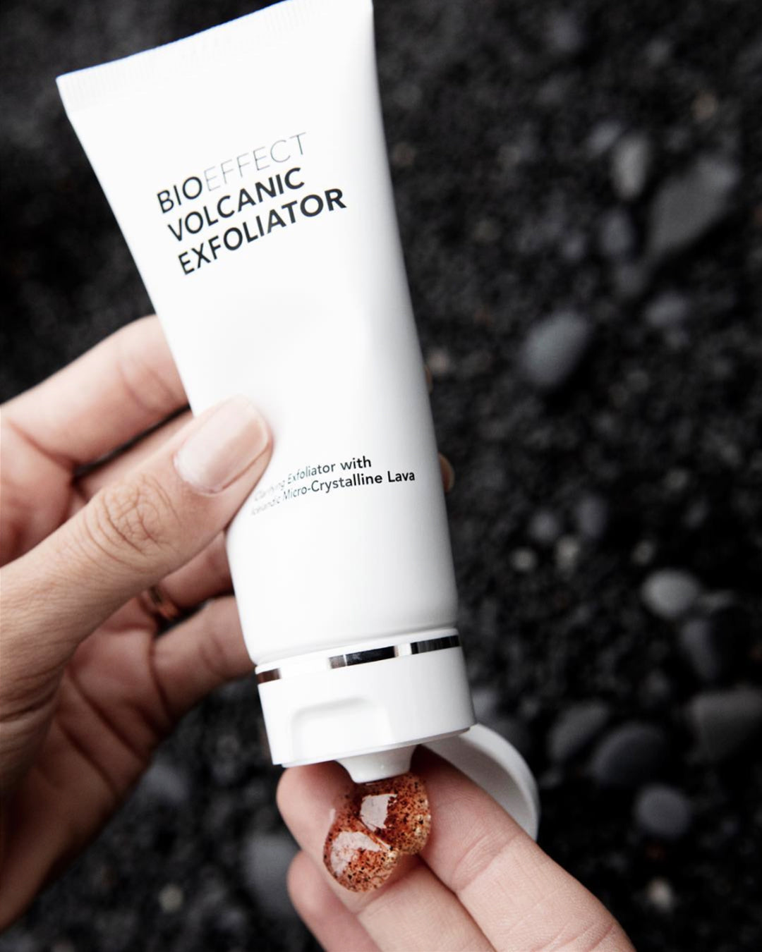 Une main applique l'exfoliant volcanique Bioeffect. La texture gel translucide aux microcristaux de lave apparait sur le doigt, prete a etre masse sur la peau.