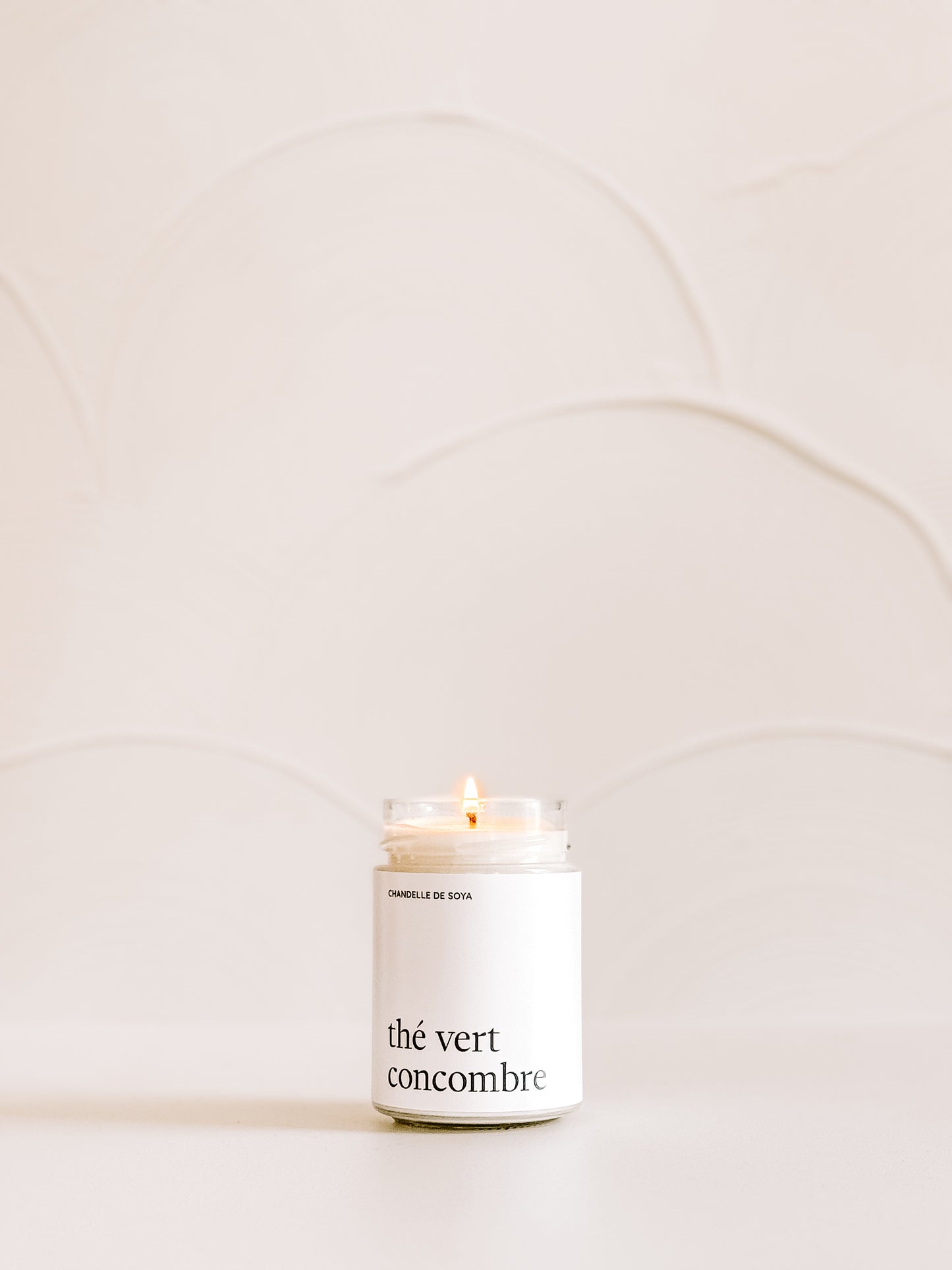 Une chandelle de soya the vert concombre illuminee, placee sur une surface claire avec un decor minimaliste en arriere-plan.