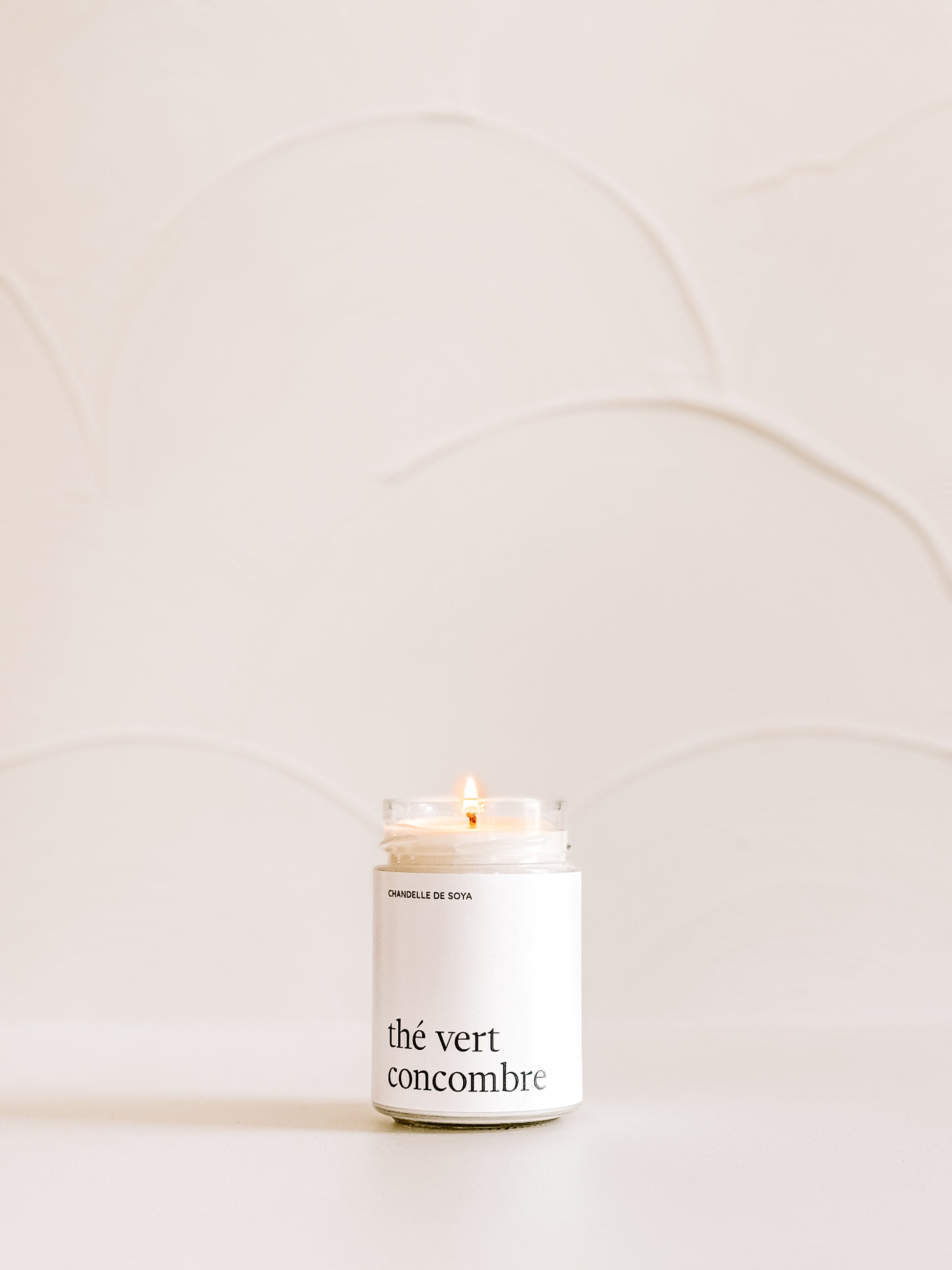 Une chandelle de soya the vert concombre illuminee, placee sur une surface claire avec un decor minimaliste en arriere-plan.