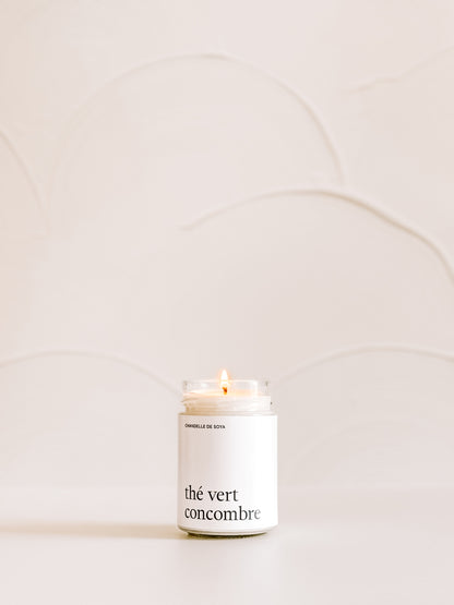 Une chandelle de soya the vert concombre illuminee, placee sur une surface claire avec un decor minimaliste en arriere-plan.