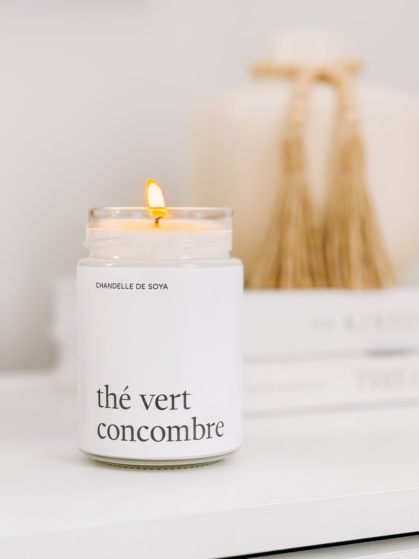 Une chandelle de soya the vert concombre illuminee, placee sur une surface avec des accessoires decoratifs naturels.