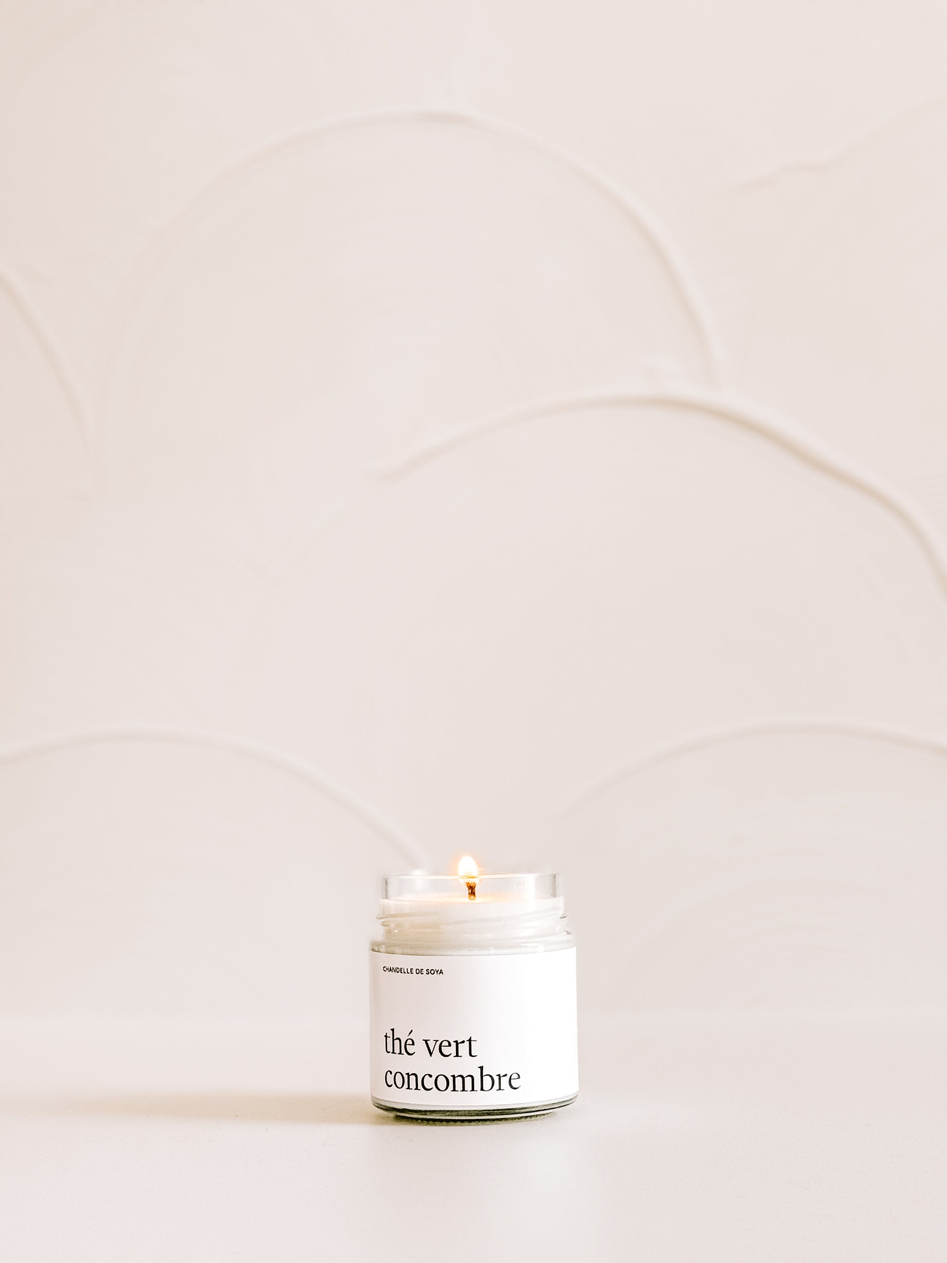 Une chandelle de soya the vert concombre illuminee sur une surface neutre avec un mur clair en arriere-plan.