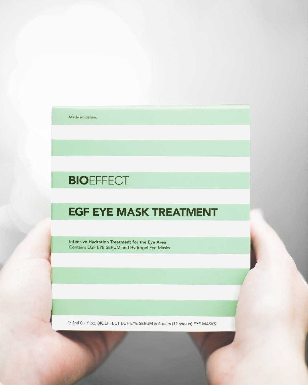 Coffret hydratant EGF Eye Mask Treatment de Bioeffect tenu dans les mains, rayures vert menthe et blanches, fabriqué en Islande pour une hydratation ciblée du contour des yeux.