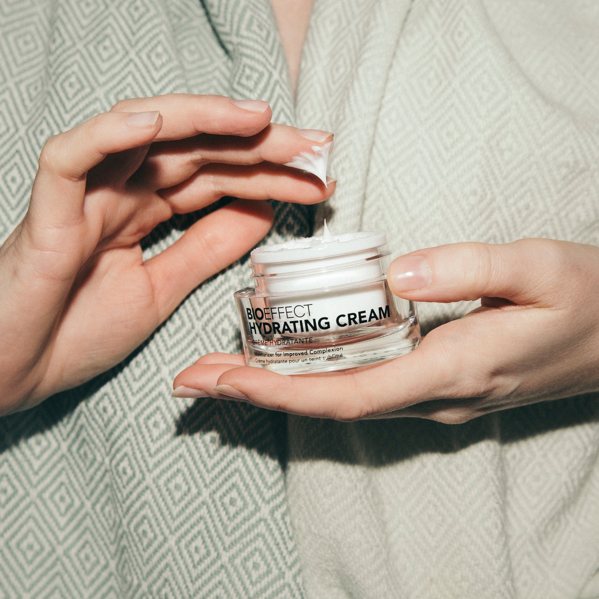 Gros plan sur une femme appliquant la crème hydratante Bioeffect avec ses doigts, révélant une texture riche et onctueuse dans un pot de verre transparent. Ambiance douce et cocooning.