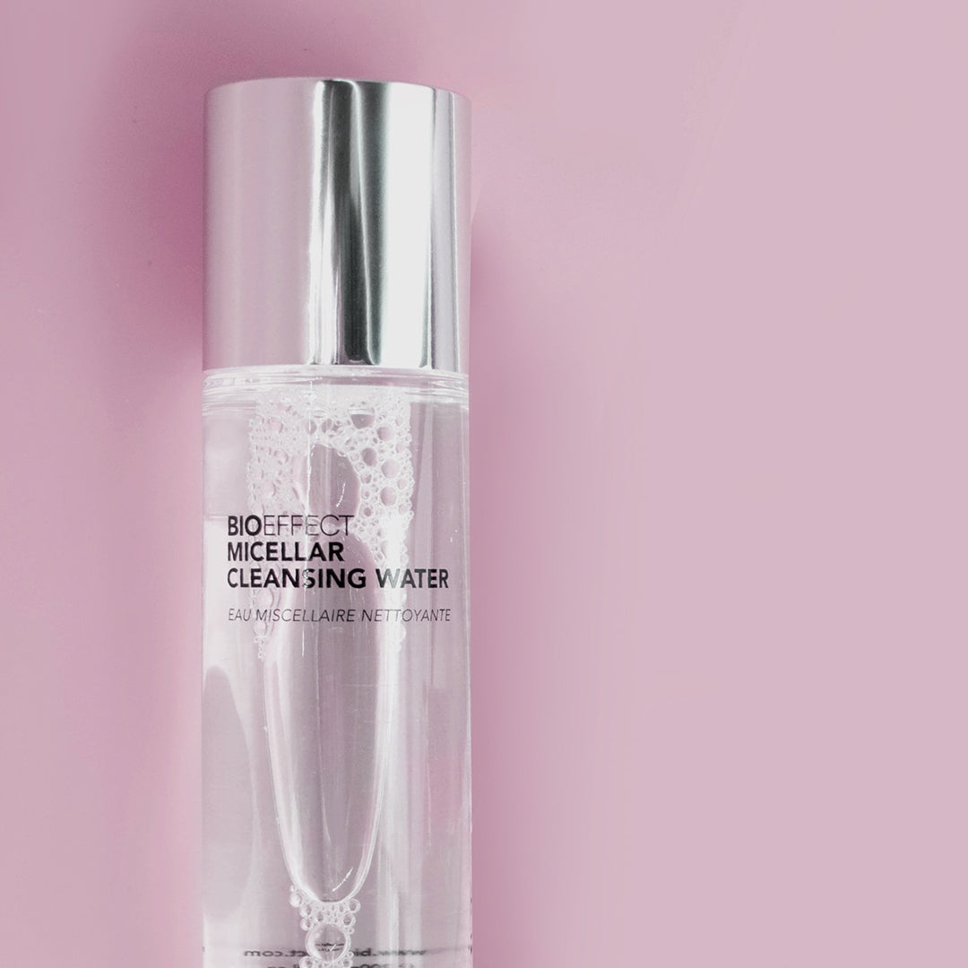 Flacon transparent de l’eau micellaire nettoyante Bioeffect sur fond rose pastel. Le produit capture la lumière avec élégance, illustrant sa pureté et sa douceur.