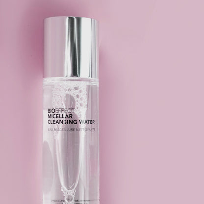 Flacon transparent de l’eau micellaire nettoyante Bioeffect sur fond rose pastel. Le produit capture la lumière avec élégance, illustrant sa pureté et sa douceur.