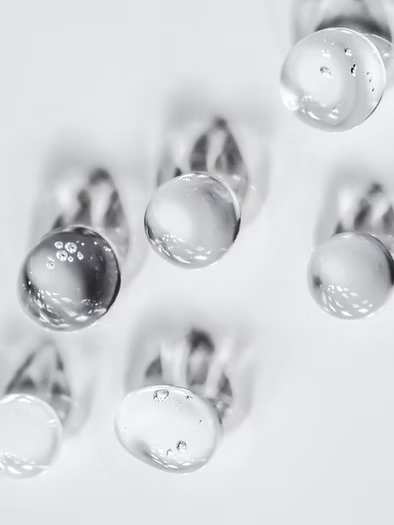 Gros plan sur une micro-goutte du serum EGF corps, reflets nacres en suspension sur la peau, mettant en valeur la purete et la richesse de la formule.