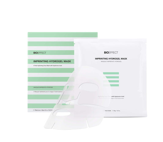Un masque en hydrogel transparent pour le visage présenté devant son emballage individuel Bioeffect Imprinting Hydrogel Mask, à côté de la boîte rayée verte de la marque.