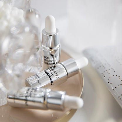 Trois flacons du traitement Bioeffect 30 Day posés sur une assiette beige, entourés d'éléments décoratifs flous, ambiance douce et raffinée.