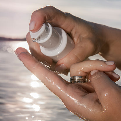 Application d’un sérum EGF corps luxueux au bord de l’eau, avec une goutte précieuse sur le bout du doigt. Idéal pour illustrer une routine peau hydratée et régénérée.