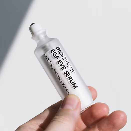 Flacon du sérum EGF Eye Serum de Bioeffect mis en scène sur un fond doux blanc-gris, avec capuchon métallique posé à côté. Application precise et regard visiblement rajeuni grâce à sa bille métallique rafraîchissante.