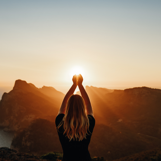 Femme contemplant un coucher de soleil, symbole de sérénité et de connexion spirituelle, évoquant l'énergie harmonisante des synergies Anges et Archanges.