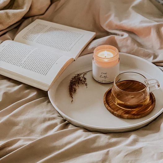 Chandelle de soya Chaï latté de Marée allumée, accompagnée d’un livre et d’une tasse de thé pour une soirée cosy.